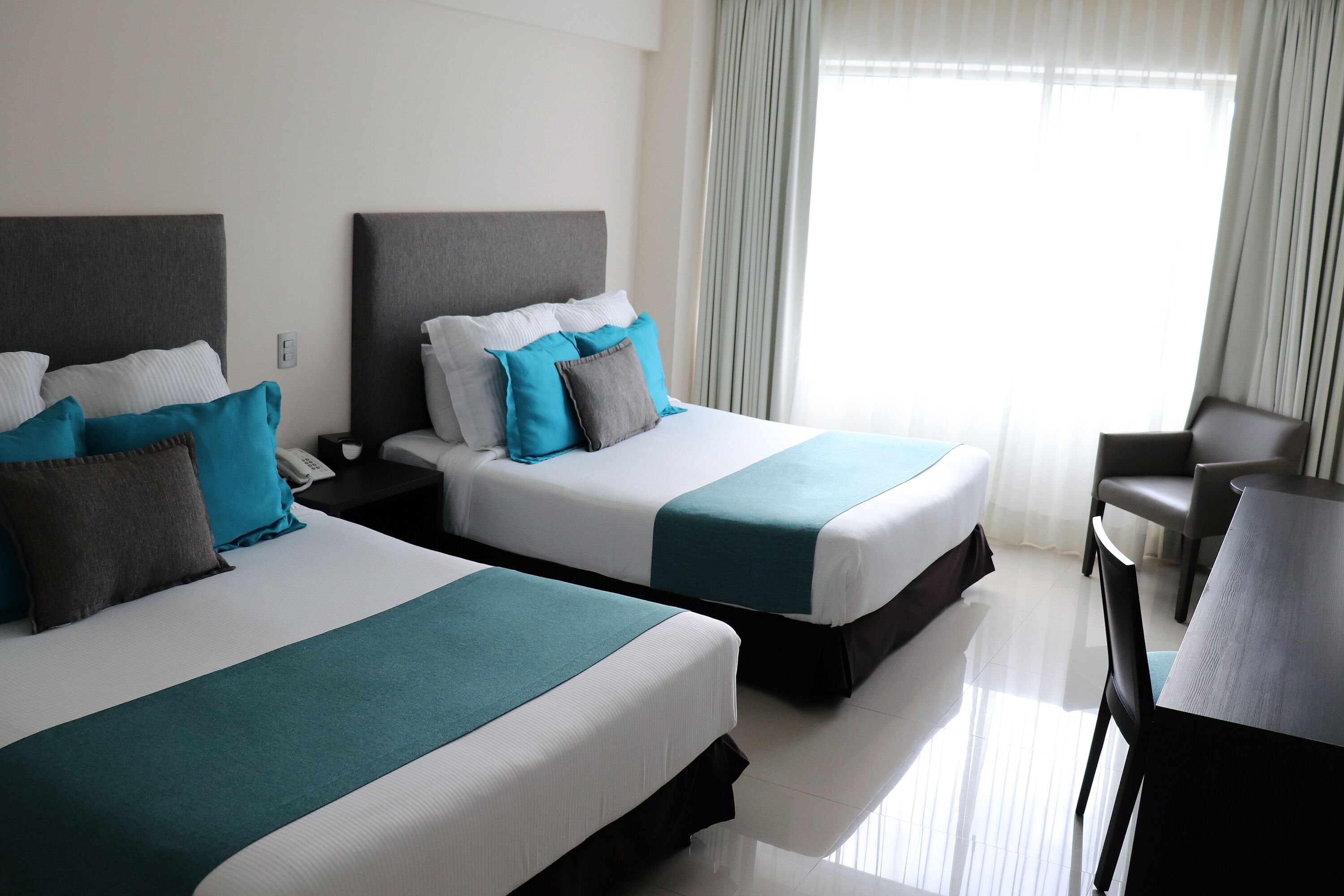 Habitació d'hotel amb dos llits, un escriptori i una cadira.