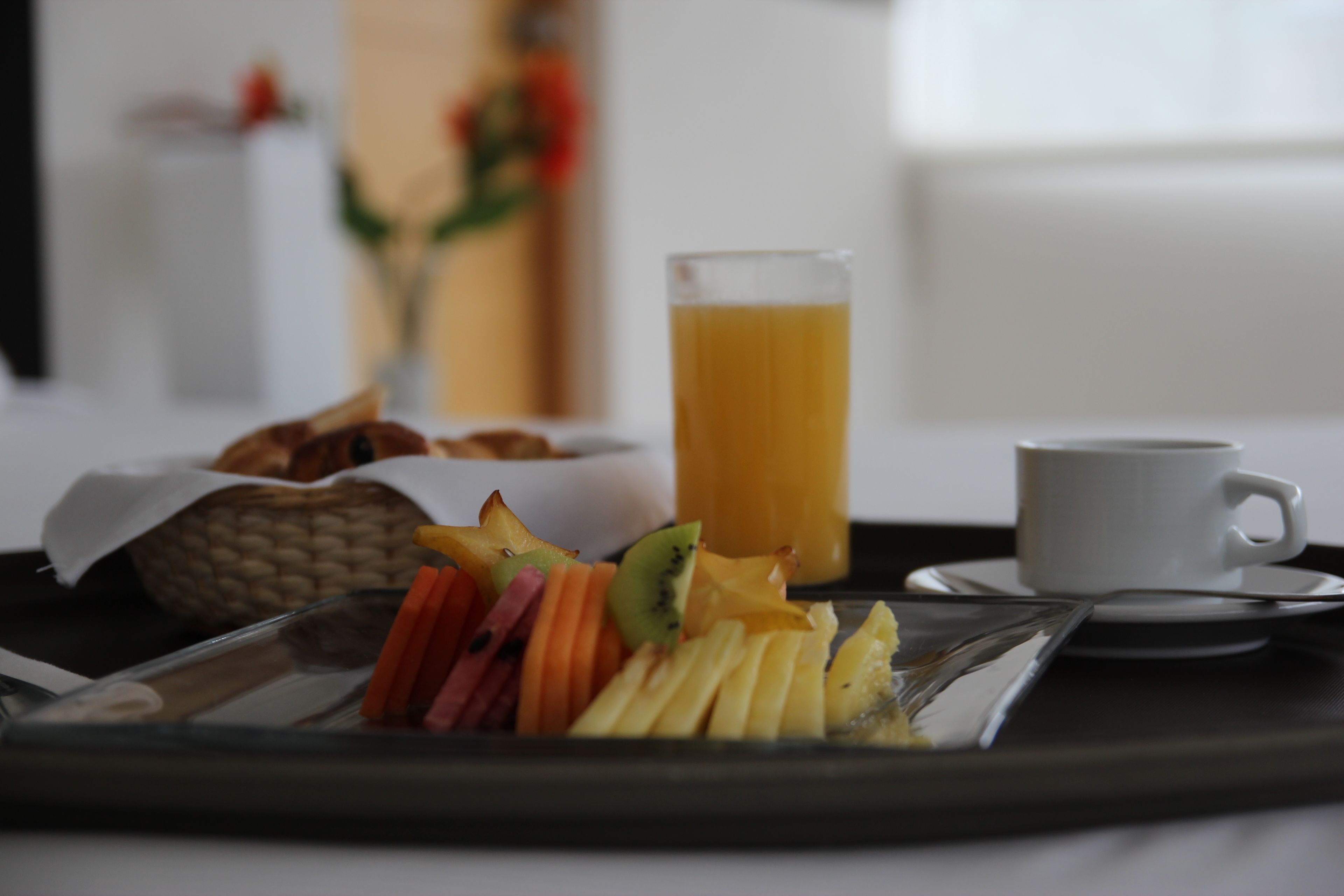 A tray with a glass of orange juice, a cup, and a plate of fruit.
