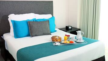 A neatly made bed with a teal bedspread, white and blue pillows, and a tray with breakfast items including eggs, toast, and orange juice.
