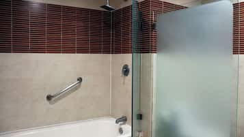 Un baño con cabina de ducha de vidrio, una bañera blanca y un pasamanos.