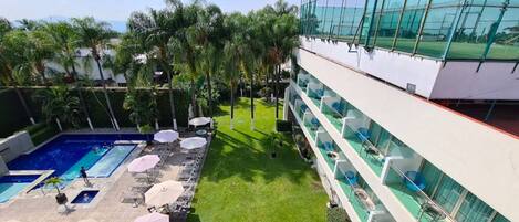 Un hotel con piscina, mobiliario exterior y vistas al entorno verde.
