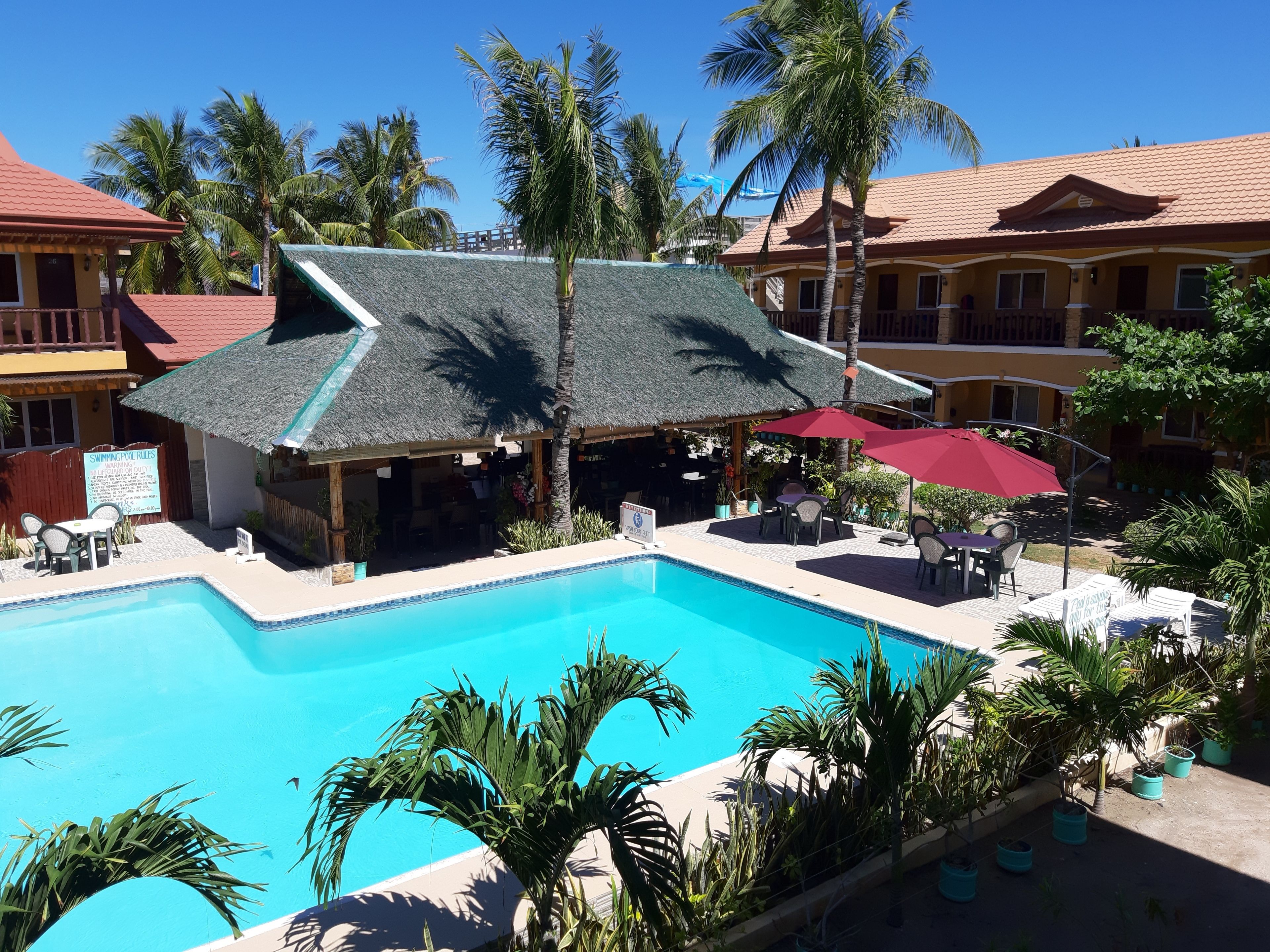A swimming pool surrounded by palm trees and a building with a tiled roof.