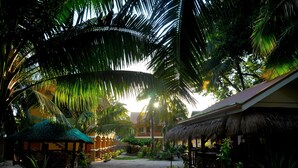 Un complexe hôtelier tropical doté de bâtiments à toits de chaume, de palmiers et d’un chemin central menant à un bâtiment avec un balcon.