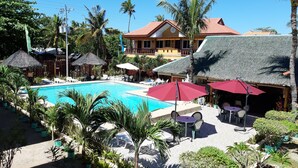 Un complexe hôtelier doté d’une piscine, de bâtiments à toits de chaume et d’une végétation tropicale.