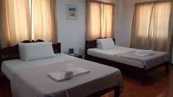A hotel room with two beds, each with white linens and pillows, a small bedside table with a lamp, and a framed picture on the wall.