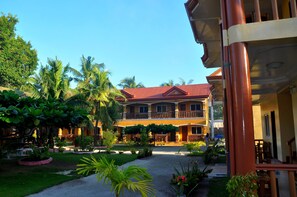 Set amidst lush greenery, this hotel features a two-story design with a balcony on the upper floor and a red-tiled roof.