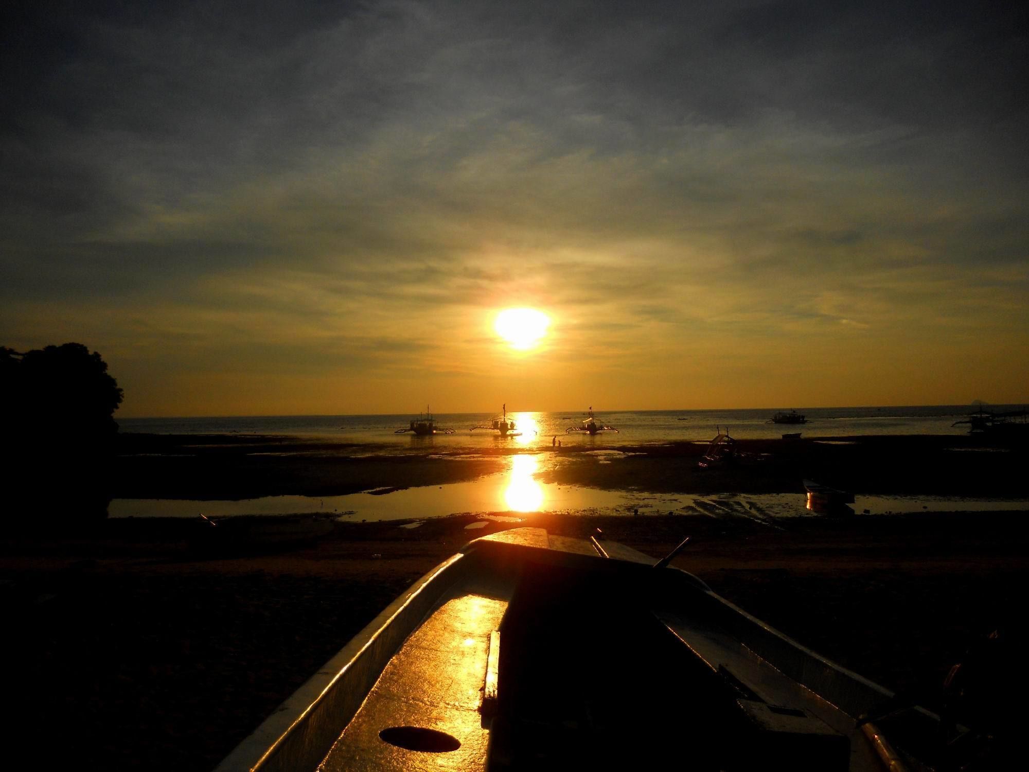 A sunset over a beach with boats and a pier.