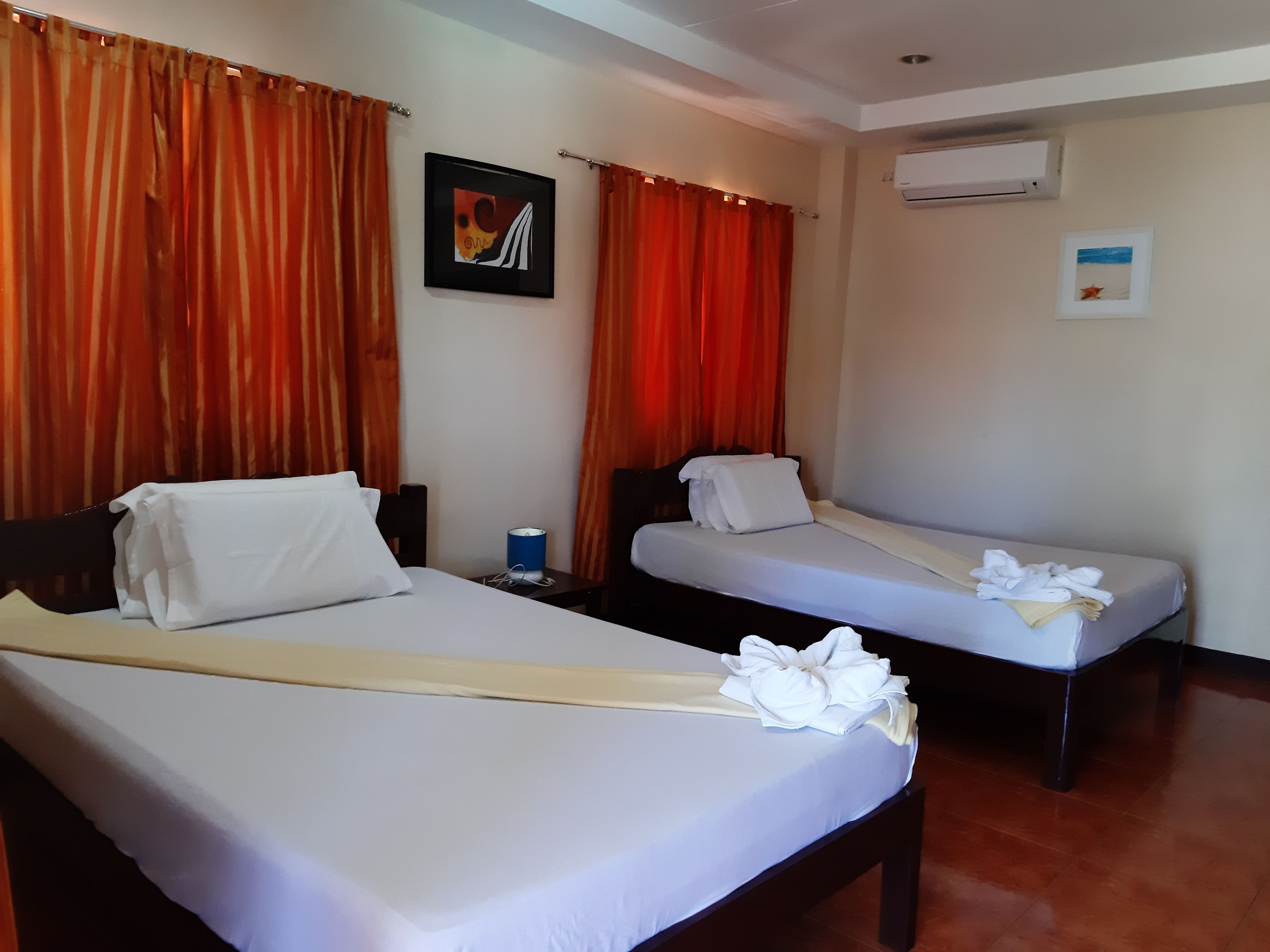 A hotel room with two beds, each with white linens and a towel on the bed. There is a framed picture on the wall and an air conditioning unit mounted on the wall.