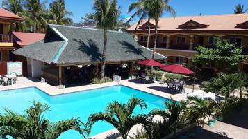 A pool area with a thatched-roof structure, outdoor seating, and palm trees.