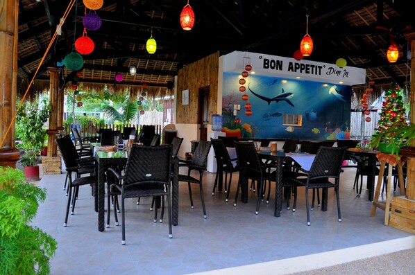 An outdoor dining area with wicker chairs and tables, a mural with marine life, and a Christmas tree. - Slam's Garden Dive Resort (Daanbantayan)