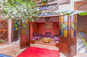 Un interno accogliente e finemente decorato, con un tappeto rosso vivace, una zona salotto con divanetti e una parete ornamentale con motivi geometrici.