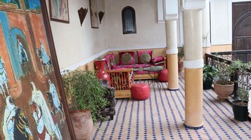Un interior tradicional marroquí con suelo de baldosas estampadas, un banco de madera con cojines y plantas en macetas.