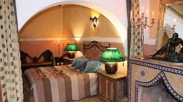 Una camera da letto con un letto, due lampade verdi, un candelabro, una statua e uno specchio decorativo.