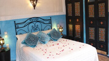 Una cama con almohadas estampadas, una lámpara de pared y una puerta decorativa con diseños intrincados.