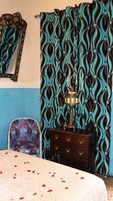 Una stanza con una tenda decorata, una lampada ornamentale, una sedia e un letto con petali di rosa.