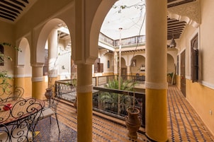Un cortile con archi, un tavolo con sedie e un lampione sospeso.