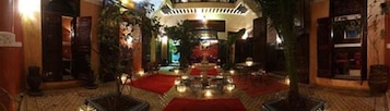 Un'hall dell'hotel con un lampadario centrale, tappeto rosso e un'area salotto con tavoli e sedie.