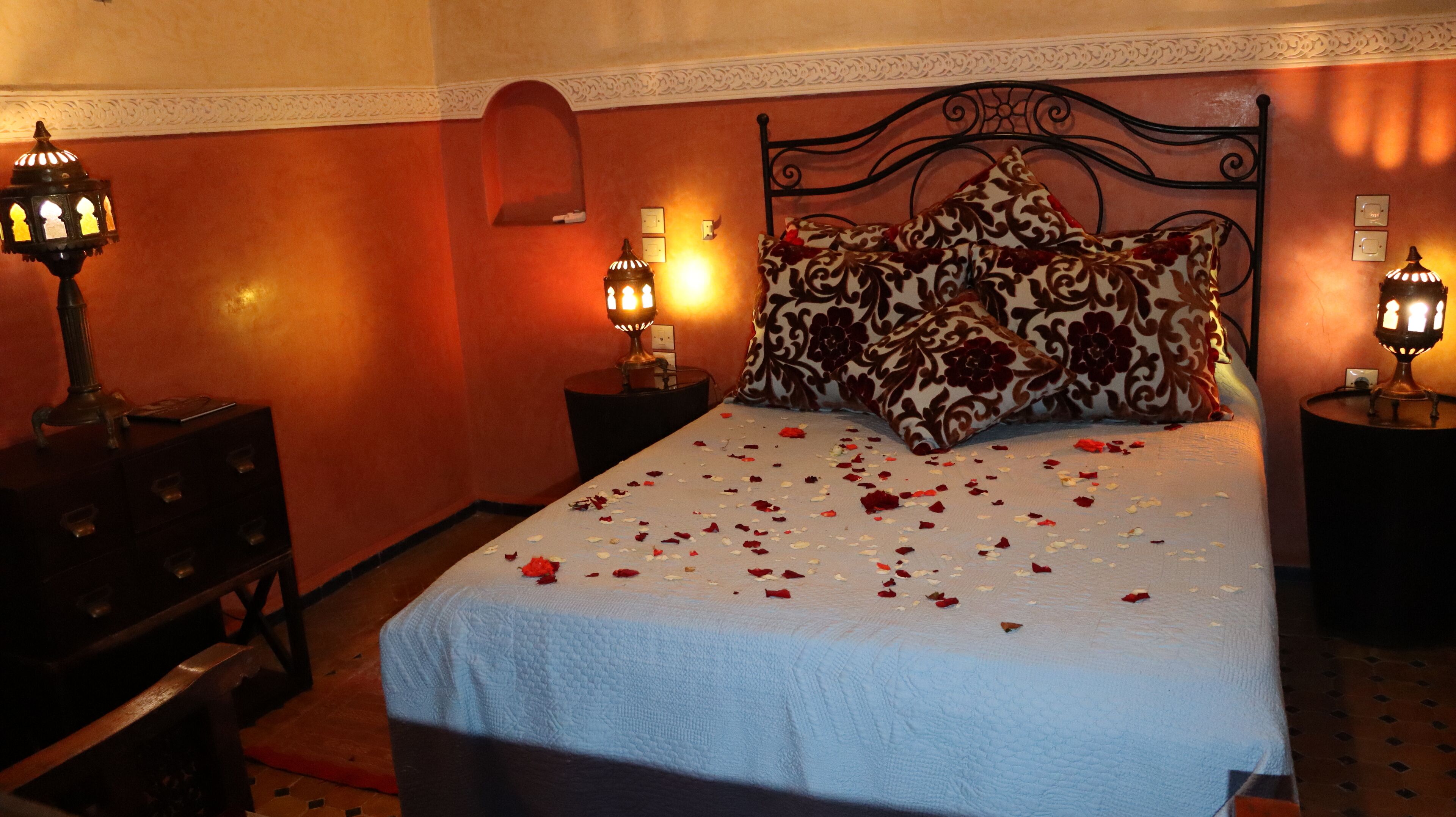 Una cama con pétalos de rosa, dos lámparas de noche y un panel decorativo en la pared.