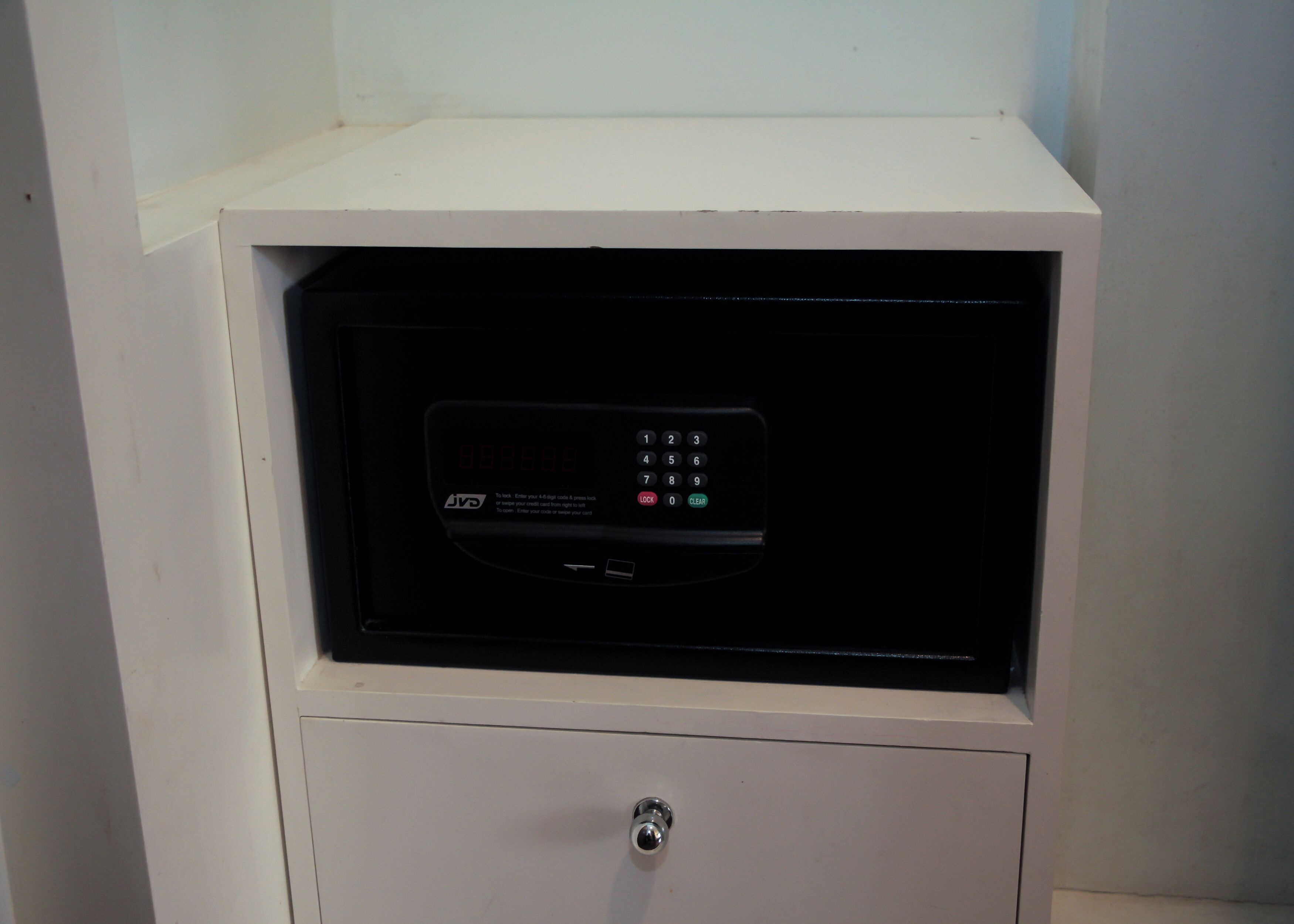 Un mueble blanco con un dispositivo electrónico negro encima, que incluye un teclado y una pantalla mostrando números.