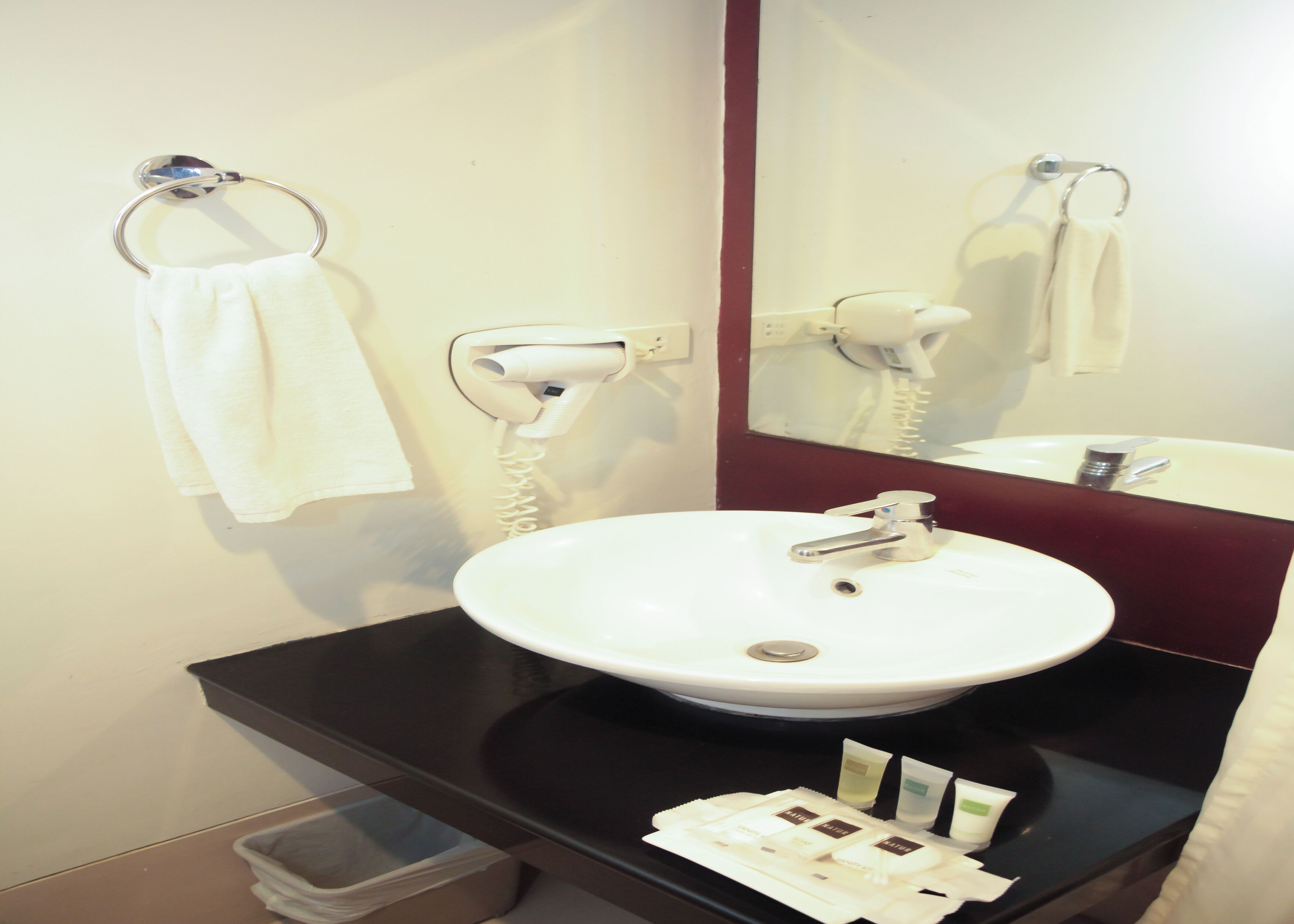 A bathroom with a white sink, a mirror, a hairdryer, and toiletries.