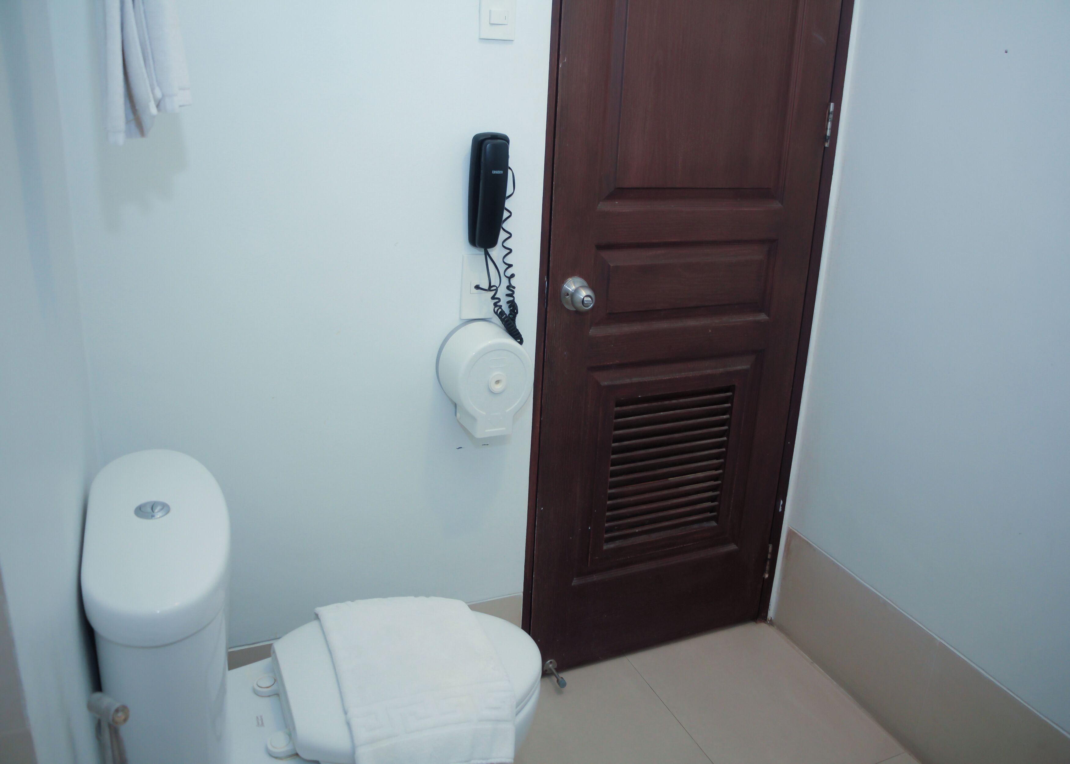 A bathroom with a toilet, a towel rack, a paper towel dispenser, and a door.