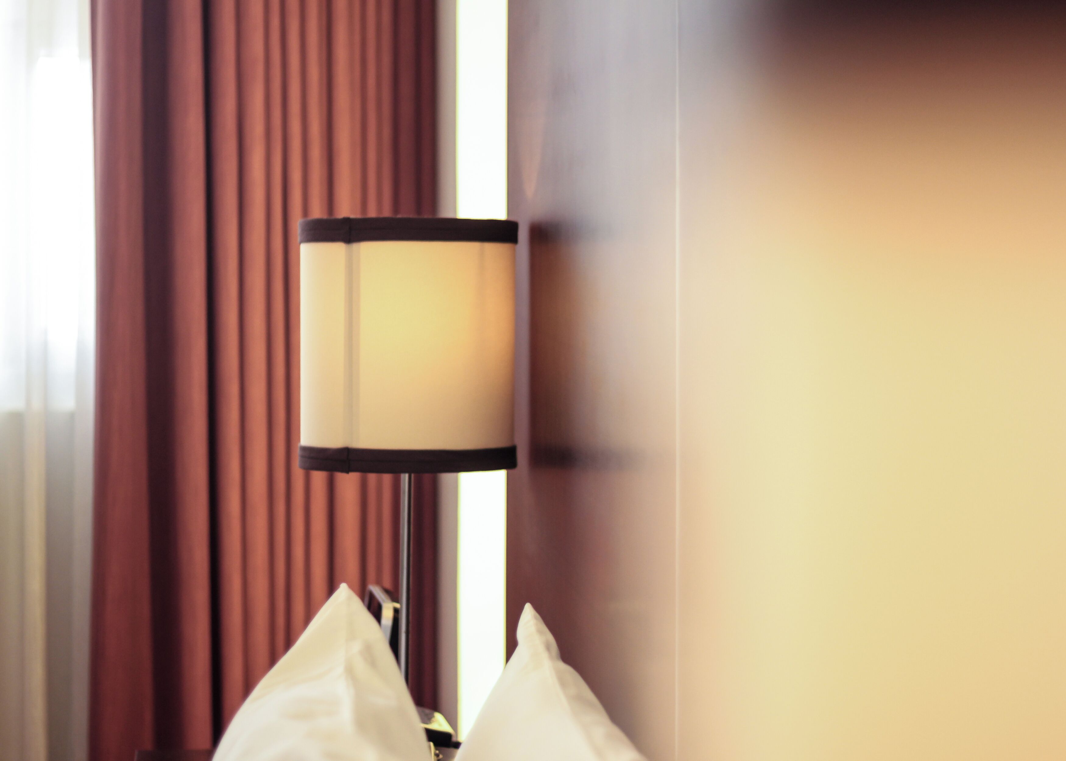 Une lampe avec un pied noir et un abat-jour beige, placée sur une table de chevet avec un coussin blanc.