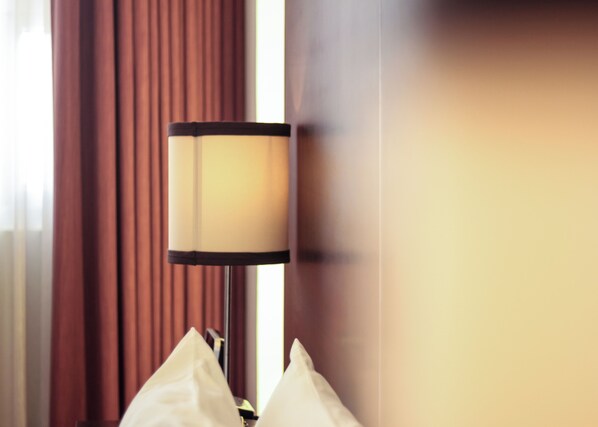 A lamp with a black base and a beige lampshade, positioned on a bedside table with a white pillow. - Casablanca Suites Near Airport (Legazpi)