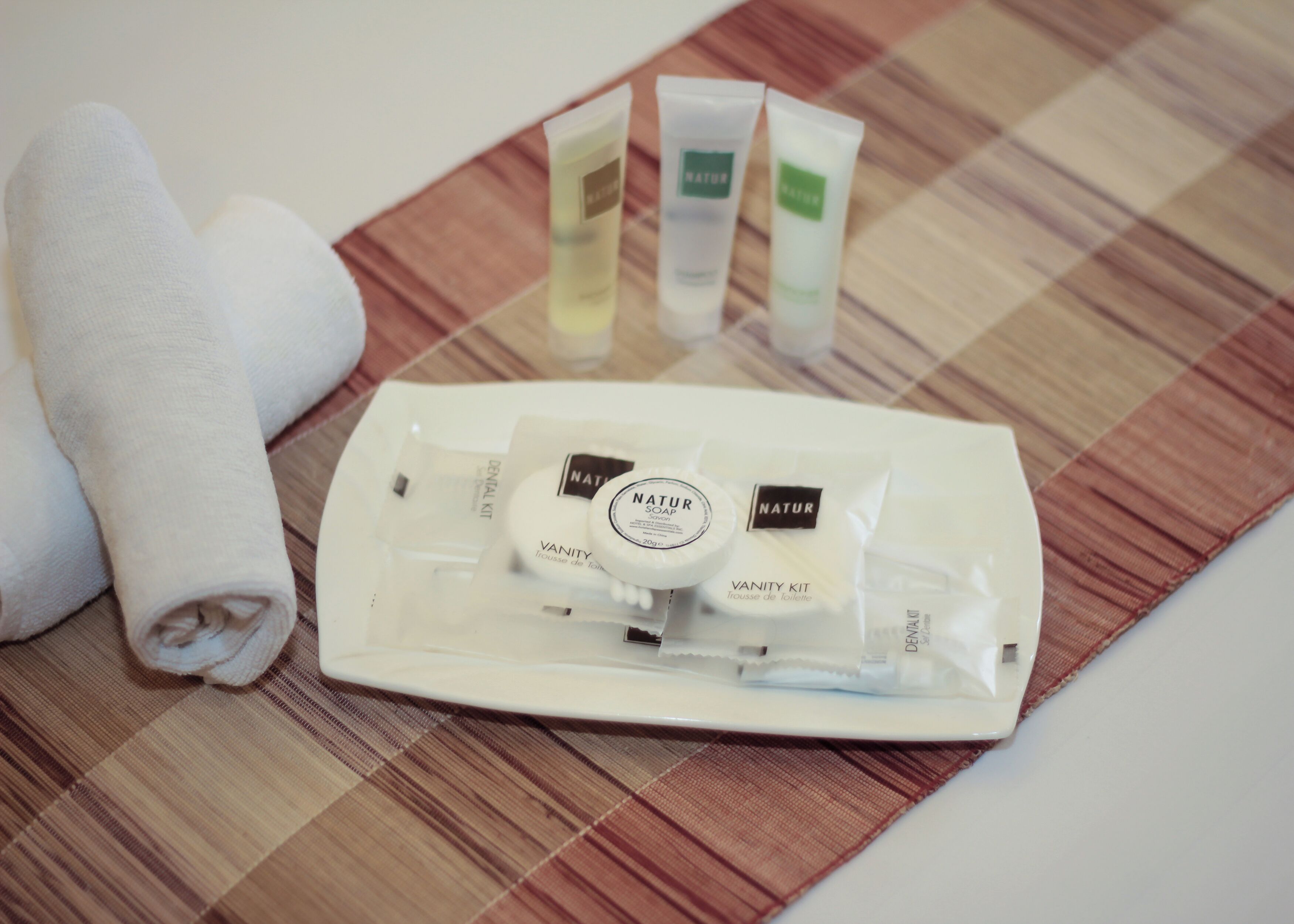 A toiletry kit with a toothbrush, a bar of soap, and two tubes of lotion on a checkered placemat.