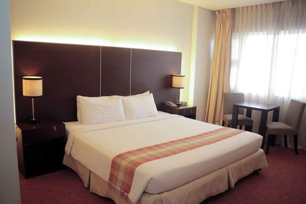 A hotel room with a large bed, two bedside lamps, a desk, and a chair.