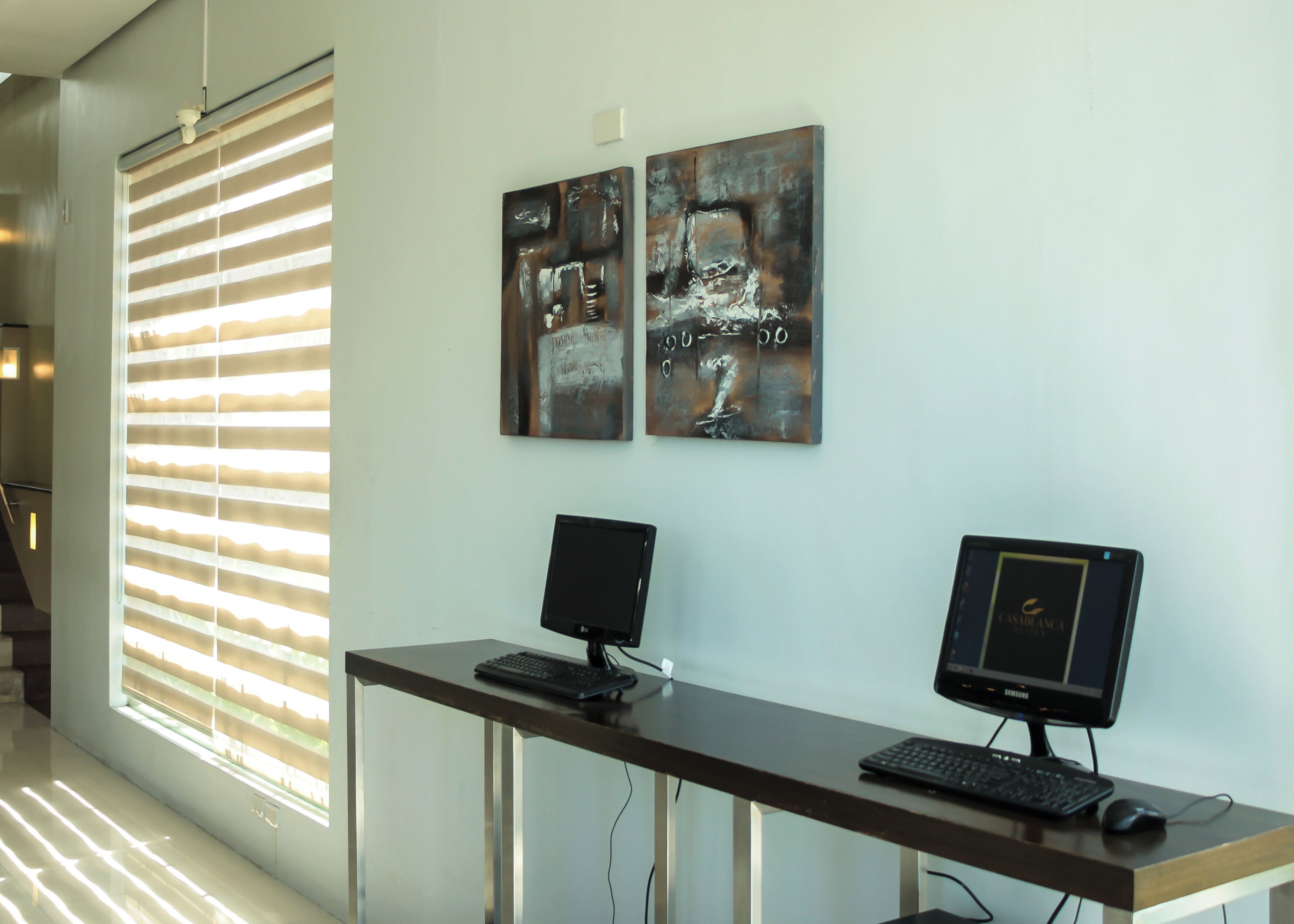 Un espacio de oficina moderno con dos monitores en un escritorio, un teclado y un ratón. Hay obras de arte abstractas de metal en la pared.