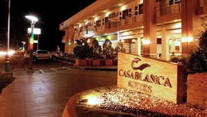Un hotel llamado "CASABLANCA SUITES" con un letrero, iluminación exterior y un área de entrada pavimentada.