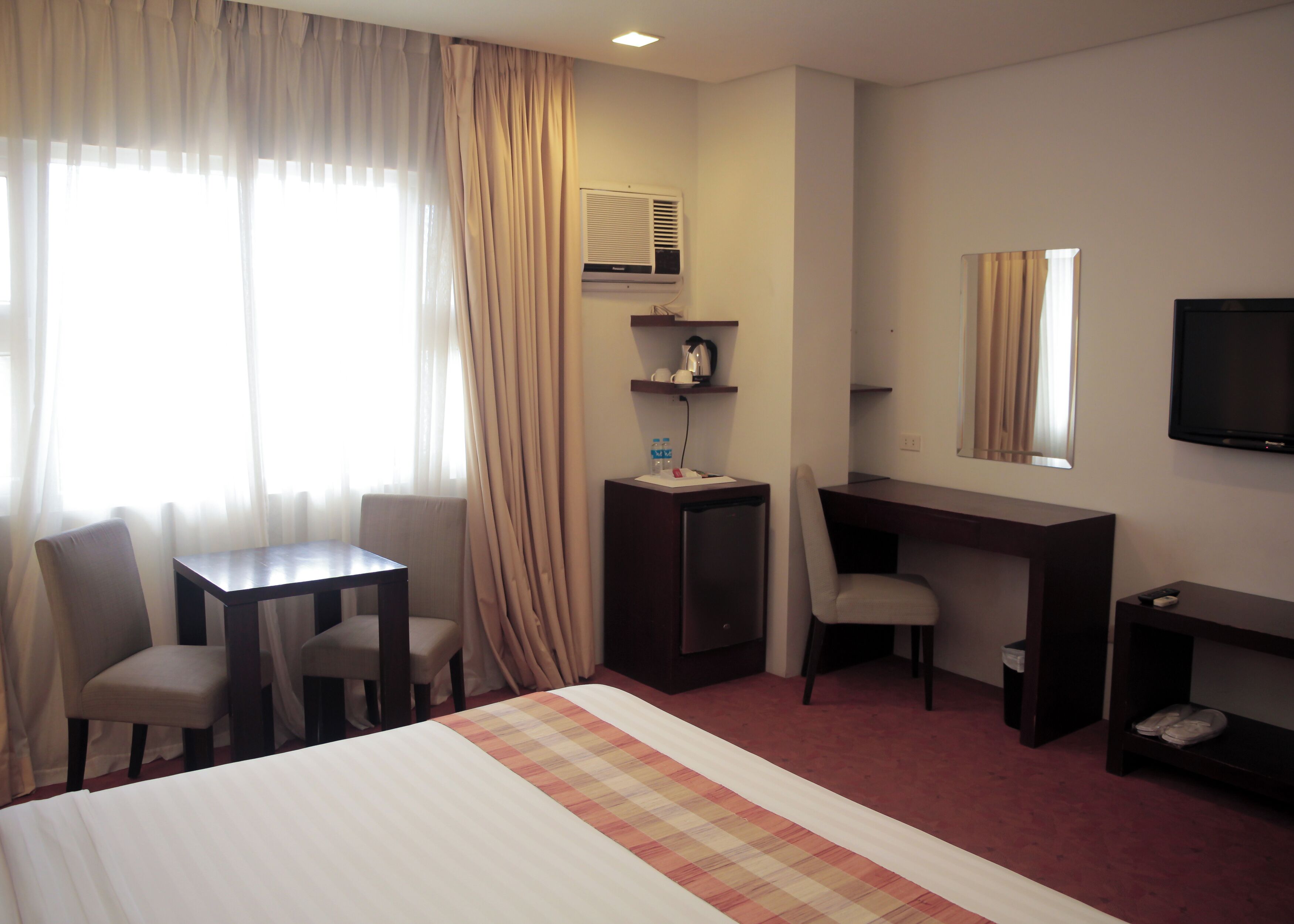 Une chambre d’hôtel équipée d’un lit, d’un bureau, de deux chaises, d’une télévision et d’un mini-bar.