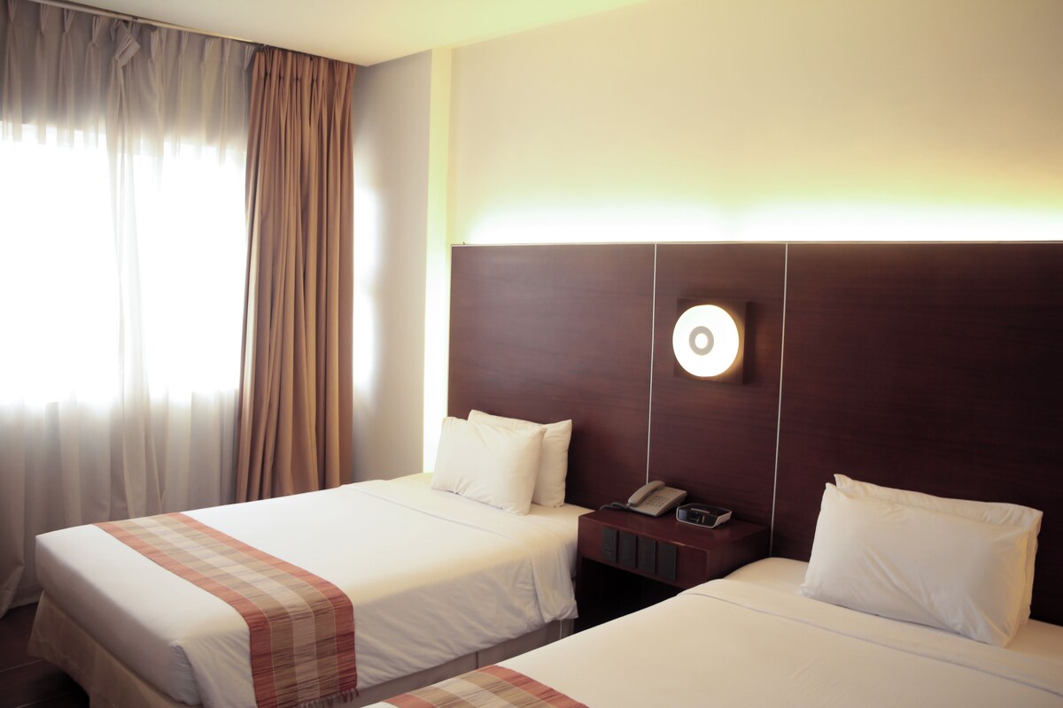 A hotel room with two beds, a bedside table with a phone, and a wall-mounted light fixture.