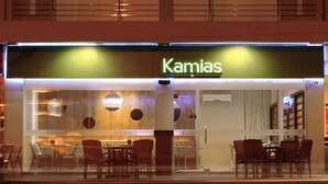 Un restaurante moderno llamado 'Kamias' con fachada de vidrio, interior de madera y zona de estar con mesas y sillas.