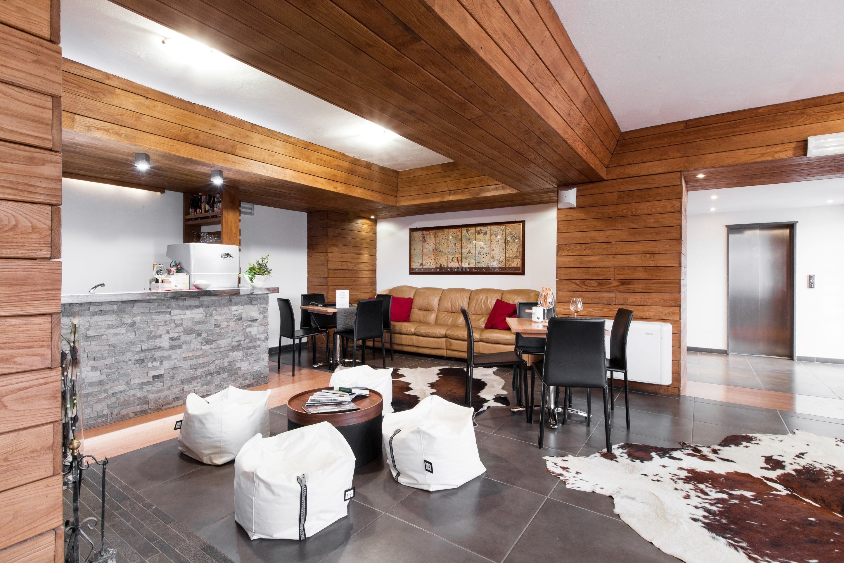 A modern kitchen with a stone island, wooden ceiling, and a dining area with a leather couch and chairs.