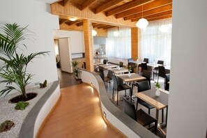 A modern restaurant with a curved wooden floor, black chairs, and a central dining table.