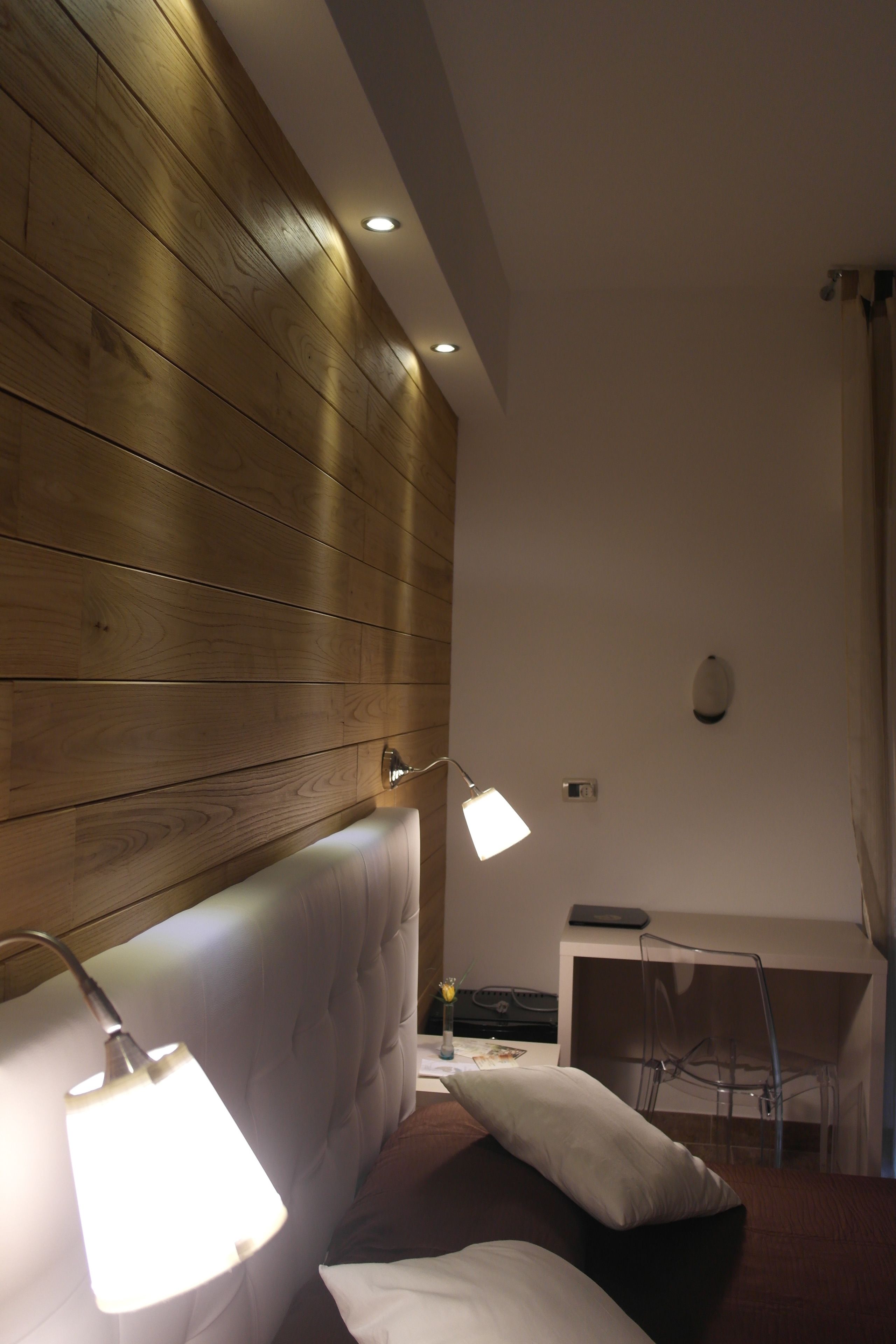 Una camera d'albergo con una testiera in legno, un letto con biancheria bianca, una scrivania con un portatile e una sedia.