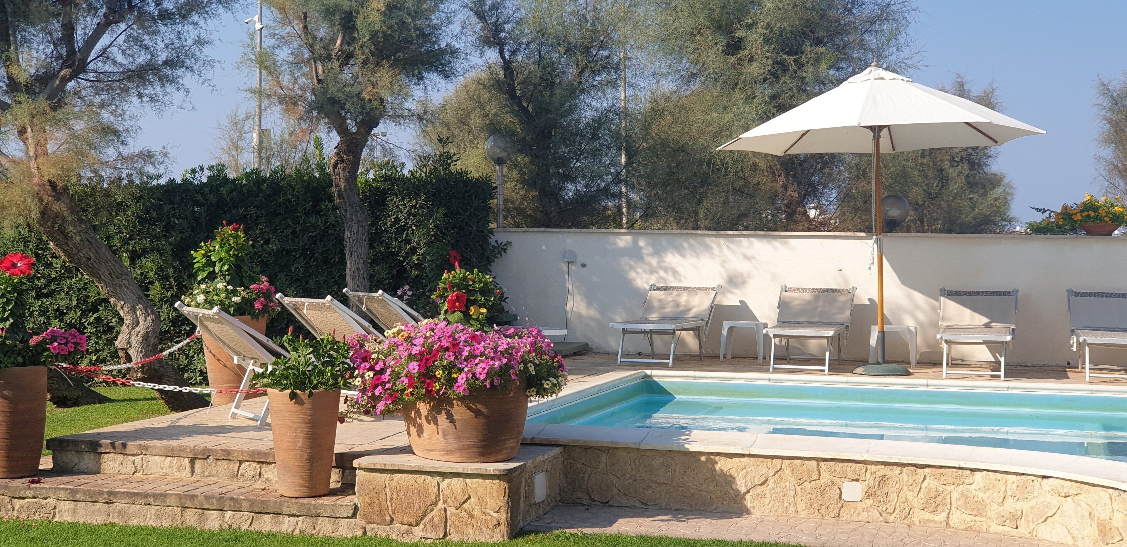 A swimming pool with lounge chairs and an umbrella, surrounded by potted plants and a stone wall.