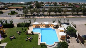 Ein Swimmingpool mit Liegestühlen und Sonnenschirmen, umgeben von einem Parkplatz und Blick auf den Ozean.