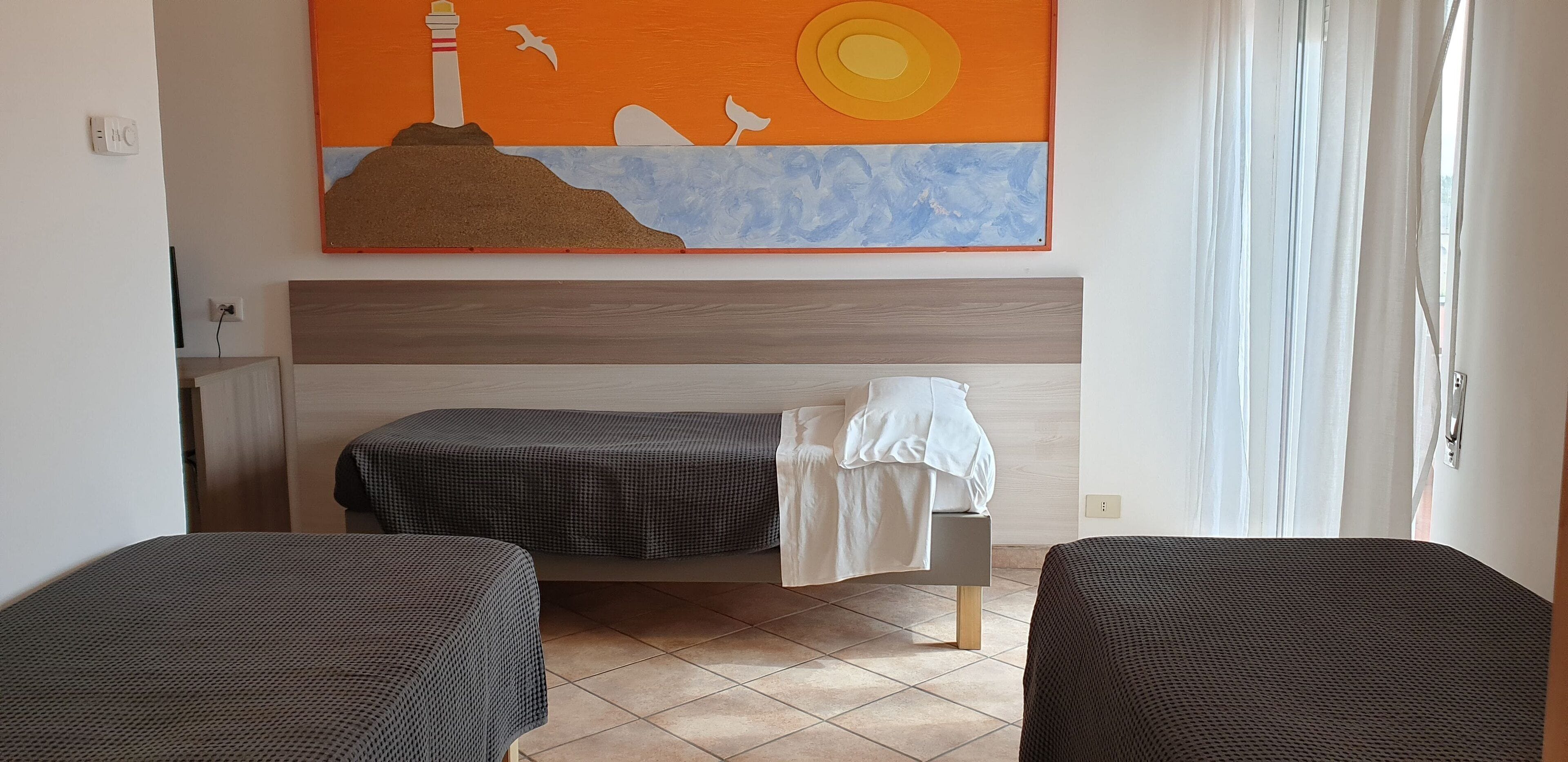 Un letto singolo con una coperta bianca, una testiera e un quadro raffigurante un faro e dei gabbiani sulla parete.