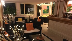 Ein modernes Wohnzimmer mit schwarzen Sofas, orangefarbenen Kissen und einem Glastisch. Es gibt eine dekorative Lichtinstallation und ein Gemälde an der Wand.