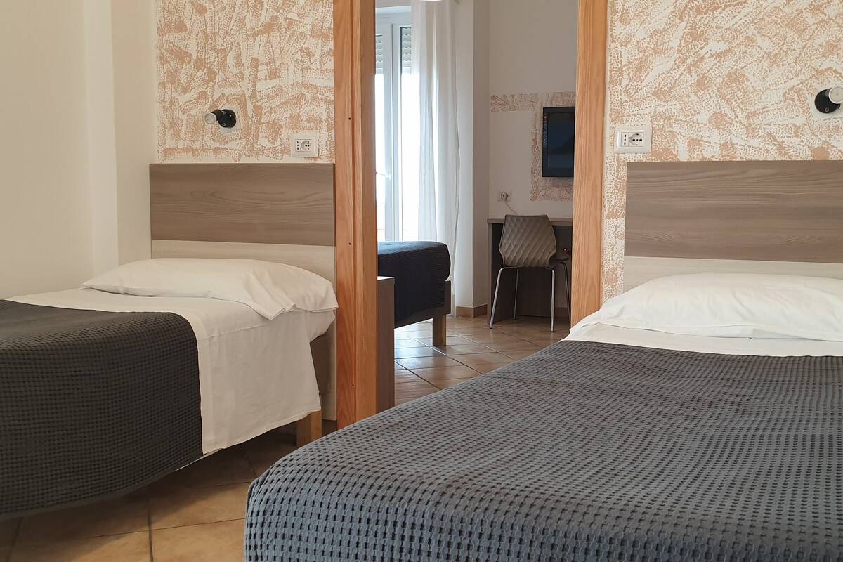 Una habitación de hotel con dos camas individuales, un cabecero de madera, un escritorio pequeño y una silla.