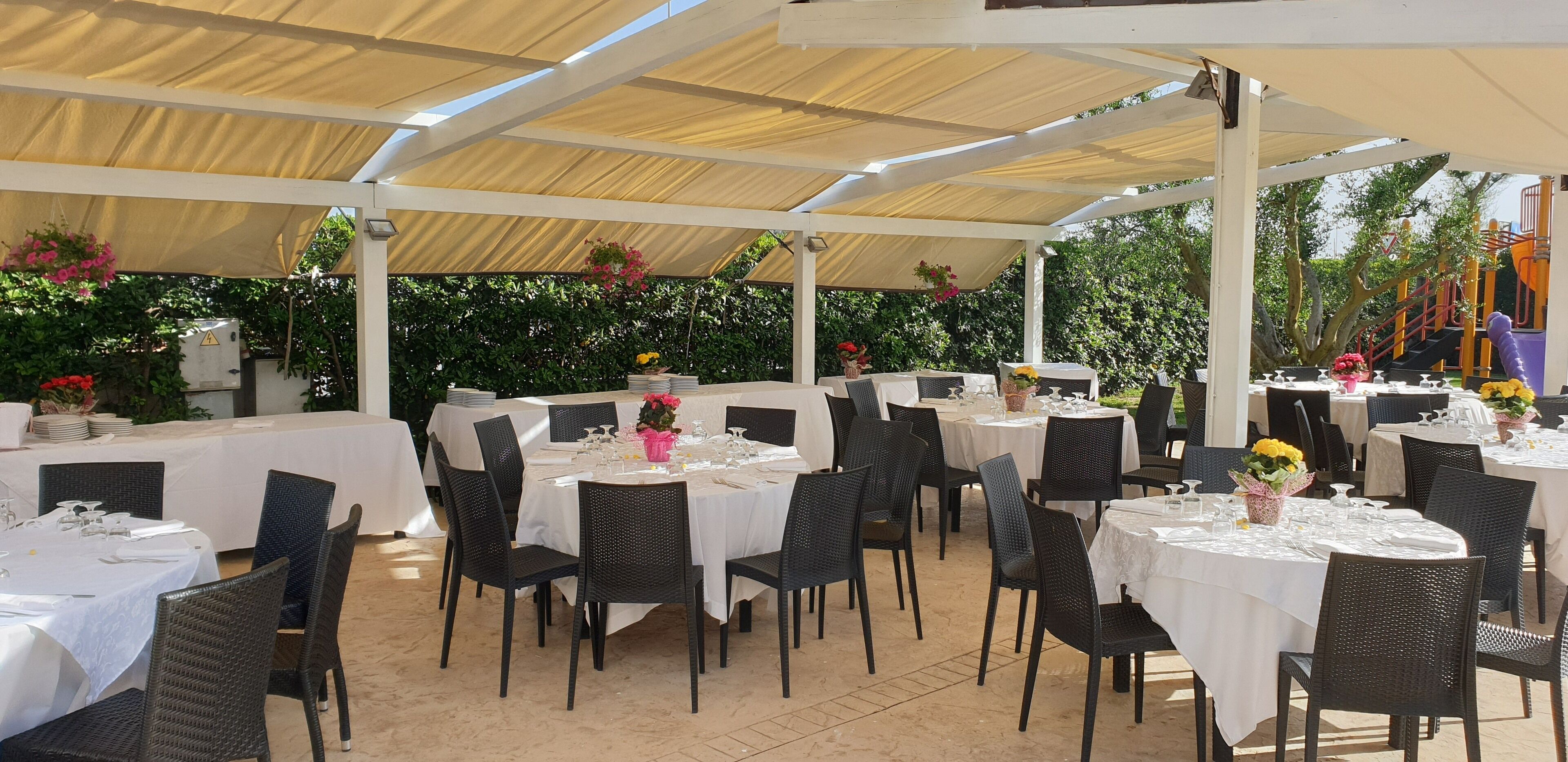 An outdoor dining area with round tables and black chairs, covered by a white canopy.