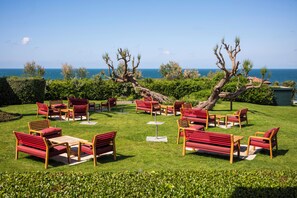 Un área de estar al aire libre bien cuidada, con muebles rojos y de madera, rodeada de vegetación y con vistas a un cuerpo de agua.