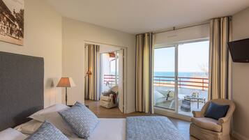 Habitación de hotel con cama, dos sillones, un escritorio y un amplio ventanal con vistas al mar.