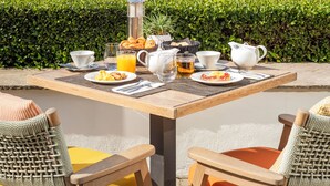 Un área de comedor al aire libre con una mesa preparada para el desayuno, sillas y vistas al mar.