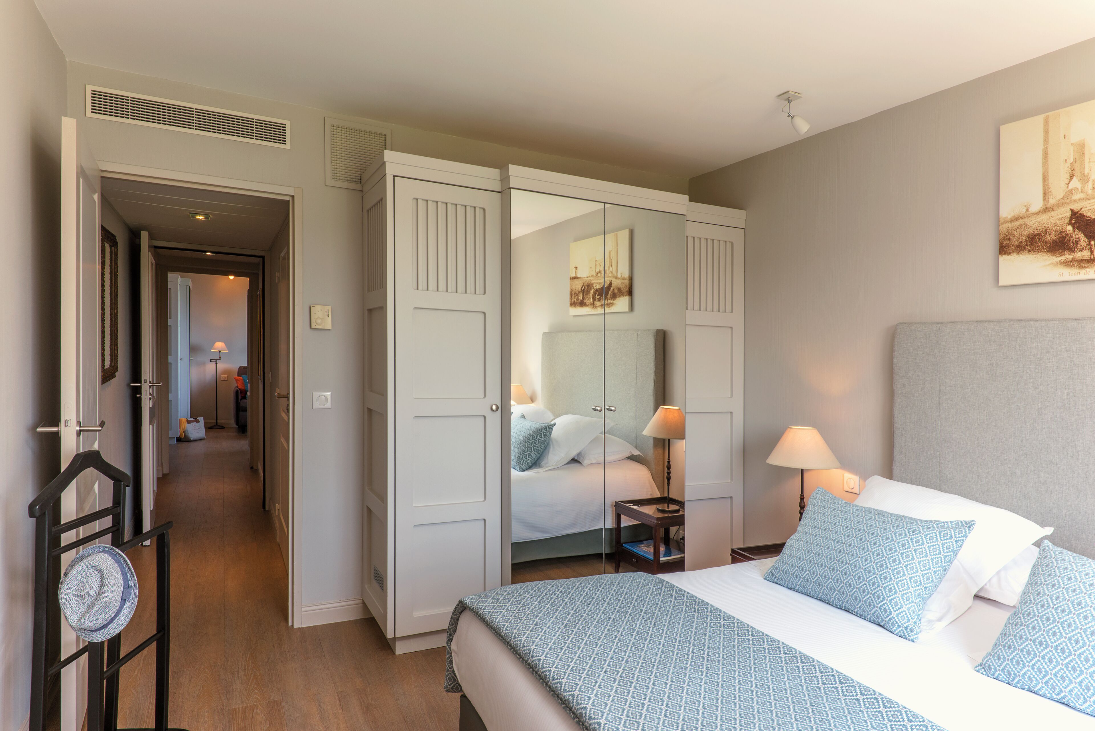 Una habitación de hotel con cama, mesita de noche, lámpara y armario con espejo.
