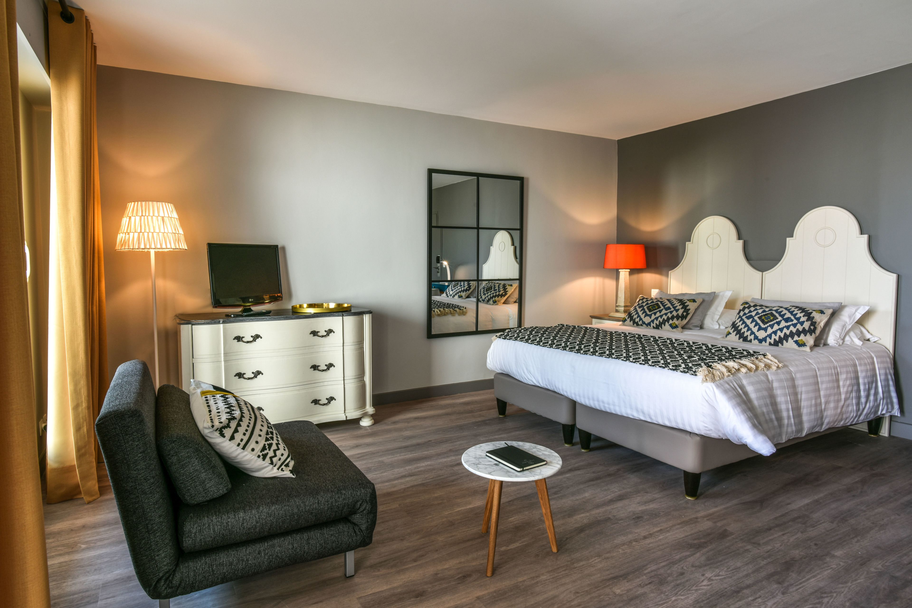 Een moderne slaapkamer met een bed, nachtkastje, lamp, televisie en een bank.