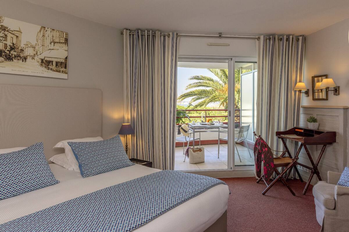 Una habitación de hotel con una cama, un escritorio y un balcón con una palmera.