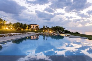 A serene pool area with a clear reflection of the sky, surrounded by lush greenery and a well-lit building in the background. - Hôtel et Résidence La Réserve (Saint-Jean-de-Luz)